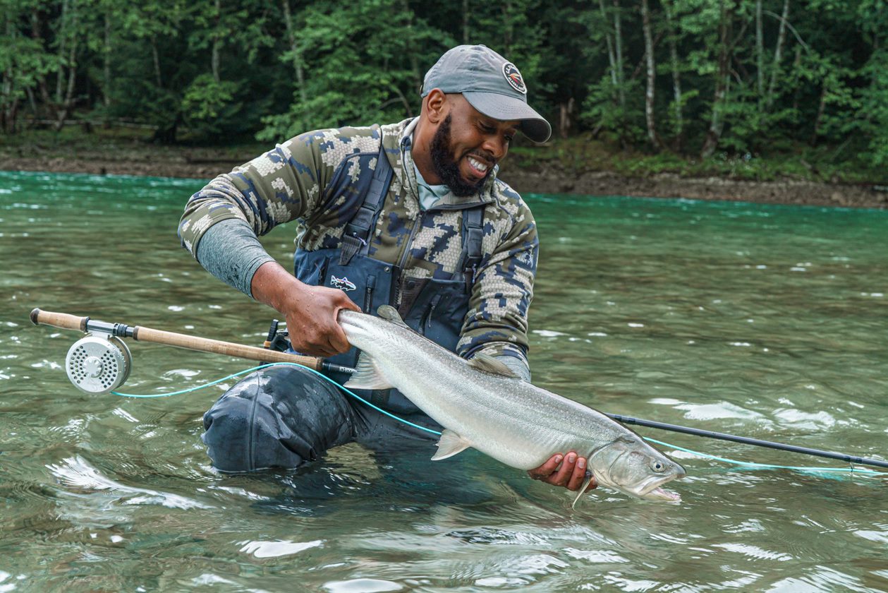 man holding large fish in stream