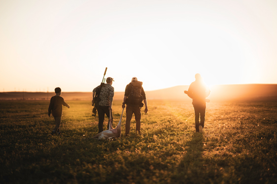 4 hunters wakling into the sunset with a deer