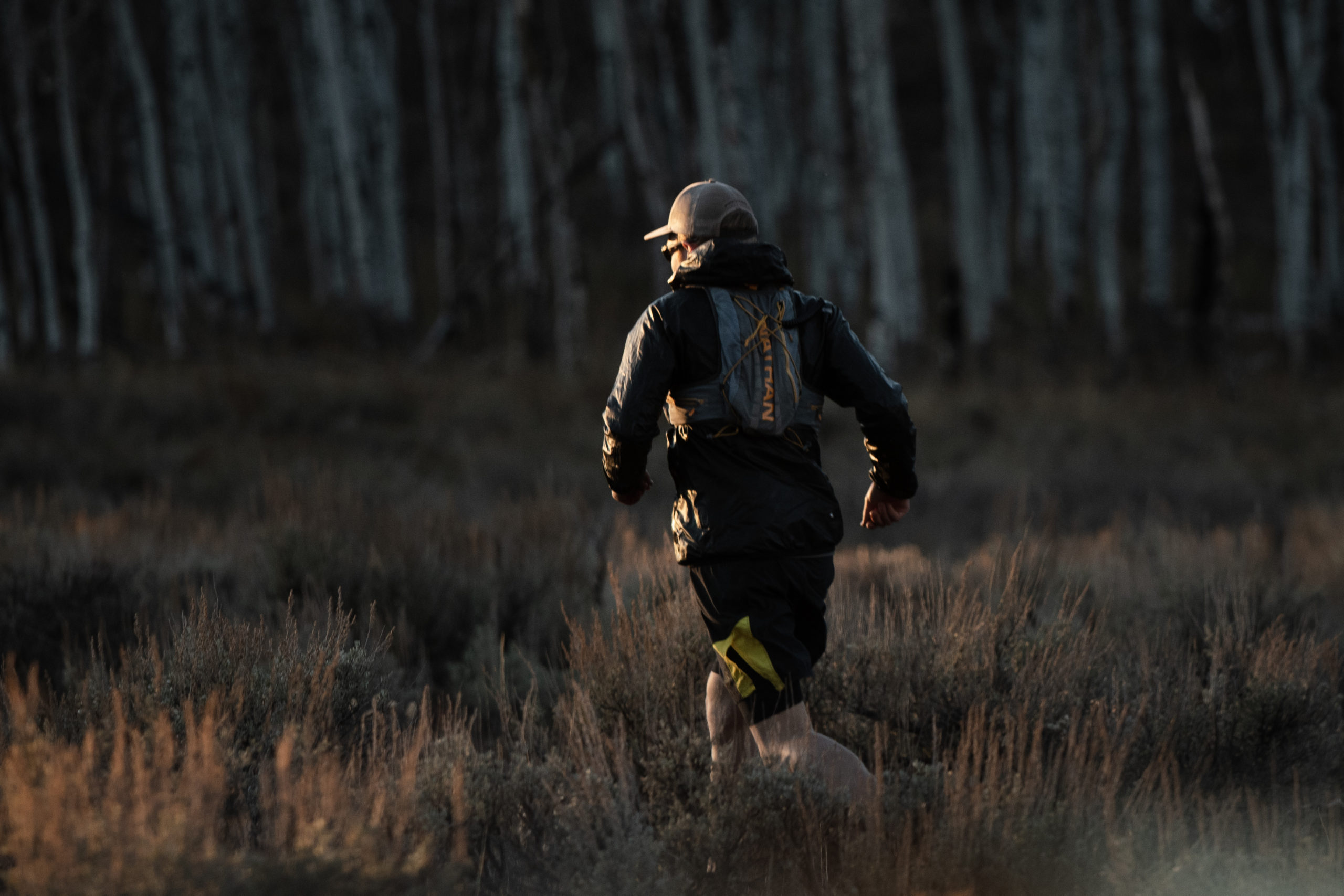 Patrick, facing away from the camer, running towards a treeline