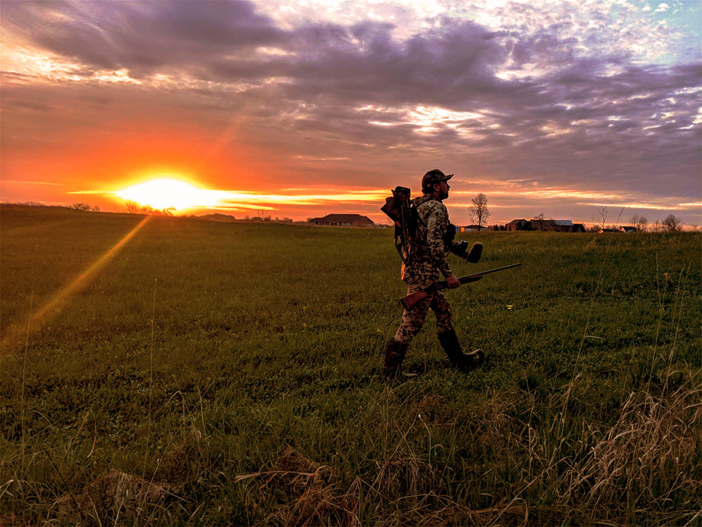Turkey hunter in a farm field at dawn
