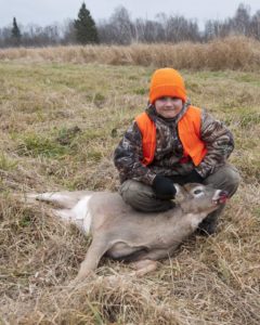 Young boy in hunting gear with deer carccass